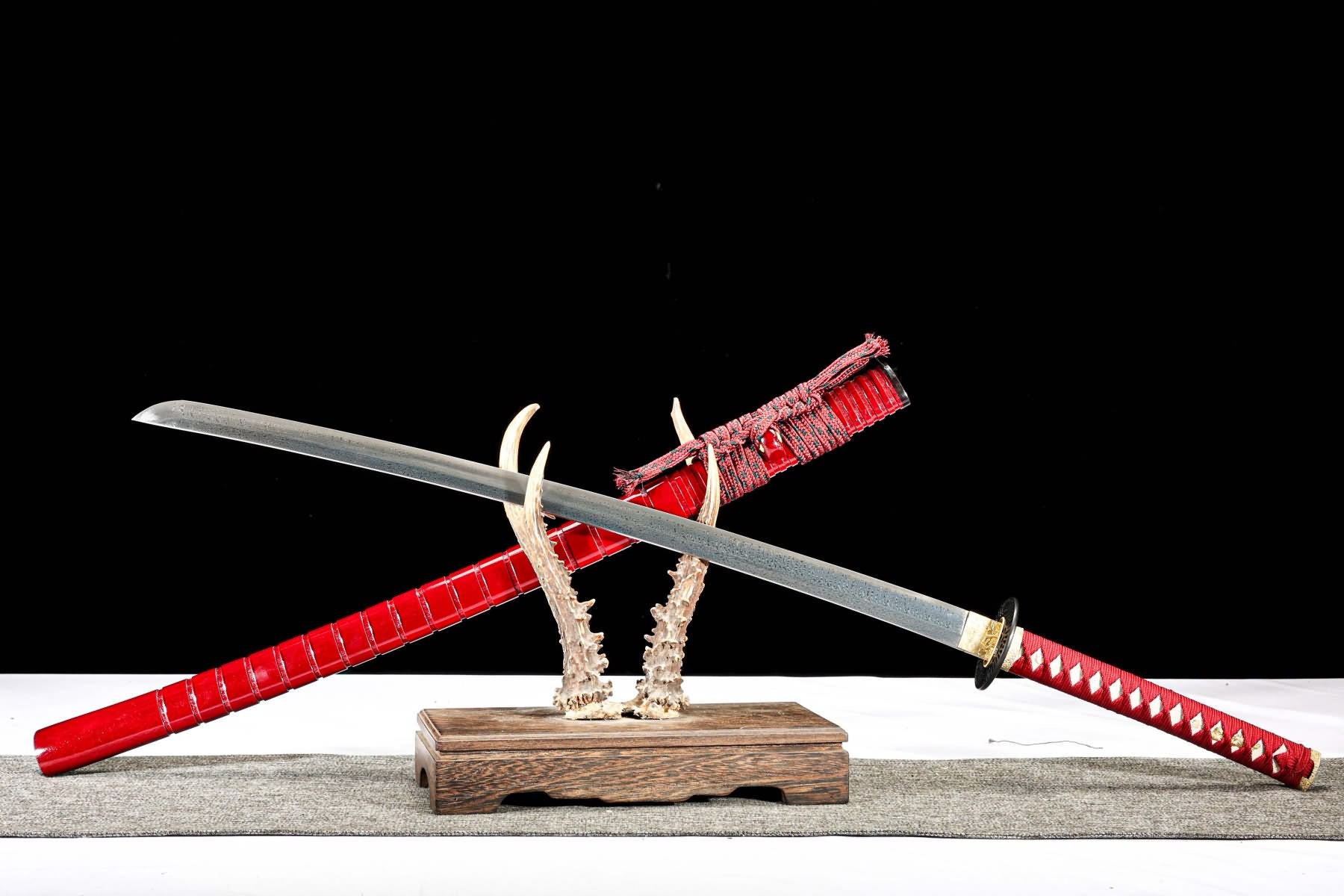 Feather-pattern katana crossed over red lacquer saya