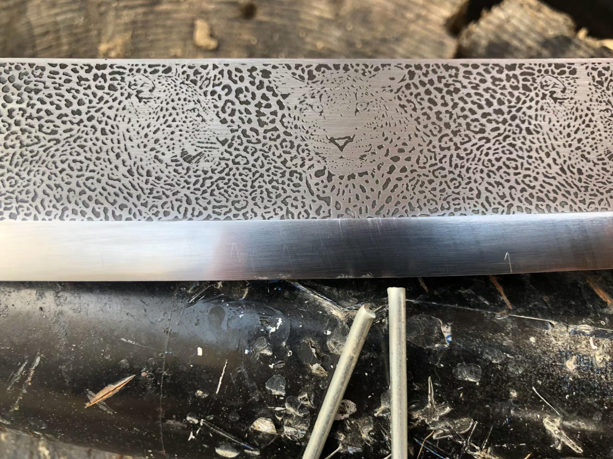 Workshop close-up showing leopard-face motifs and spots above the polished edge area of the Kangxi Dao blade